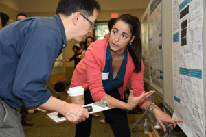 A woman gestruring and presenting her poster to a man with a clipboard
