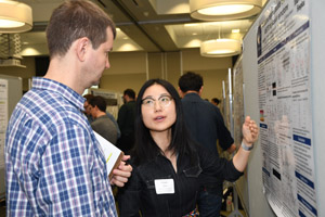 A young Asian woman presenting her poster to a man with a clipboad.
