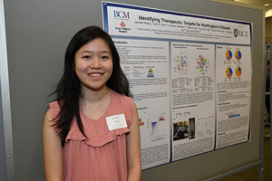 A young Asian woman smiling and proudly standing beside her poster.