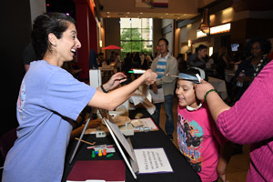 a laughing woman in a blue smock interacting with a female child exploring an exhibit together