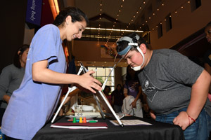 a smiling woman in a blue smock interacting with a male child as they are exploring an exhibit together