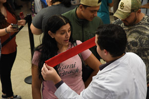 a laughing woman in a pink shirt interacting with a male in a white smock who is covering her eyes with a red blindfold.
