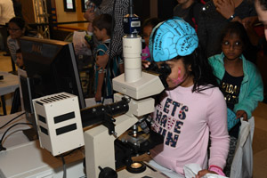a female child peering through a large microscope at a specimen of the human brain