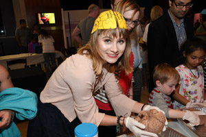 A well dressed smiling woman is holding a preserved human brain while smiling for the camera