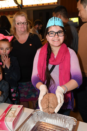 A female tween wearing a brain hat and holding a preserved human brain and smailing for the camera