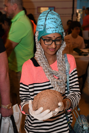 A fenmmale tween holding a human brain whilst wearing a blue brain cap