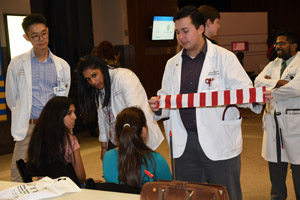 A man in a white smock showing an experiment to two young girls