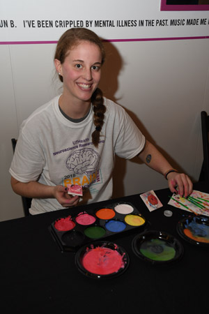 A female medical school student wearing a brain night t-shirt, applying multiple colored brain stamp tattoos to knowledge seekers
