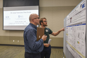 A man with a clipboard watchiing a presentation from another man presenting his poster.