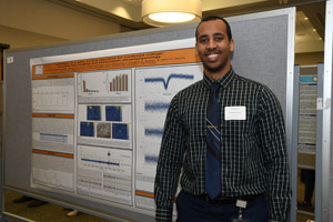 A man proudly standing beside the poster board he is presenting