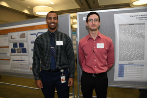 Two men standing proudly in front of their poster.