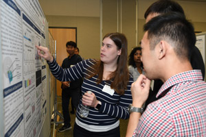 A female student explaining her poster to several men