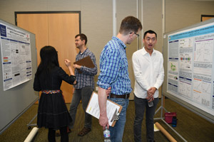 A man with a clipboard discussing a a poster with a male presenter.