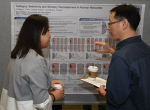 A man with a clip board asking questions of a female student about her poster