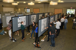 A long shot showing several rows of posters being presented and people mingling.