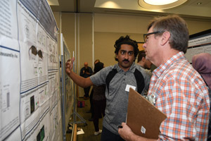 A man explaining his poster to a man with a clipboard