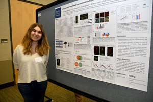 A young woman standing proudly beside her poster and smiling.