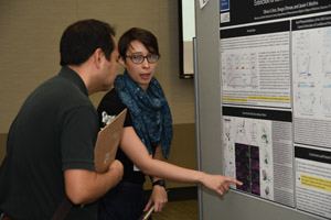 A woman presenting her poster to a man with a clipboard.