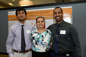 Two men with a woman between them posing for a picture in front of a poster