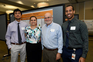 Three men and a woman posing for a picture in front of a poster