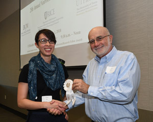 A man presenting a white winner's ribbon to a female poster presentor.