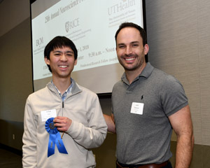 Two men standing side-by-side showing off a blue winner's ribbon
