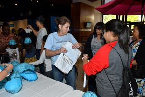 Woman and two children at a table with a person handing out blue brain skull caps