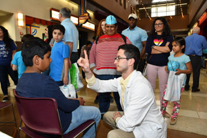 Several adults watching a man in a white smock performing perception experiments on a young boy