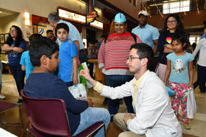 A man performing a perception experimant on a young boy with a large family unit watching