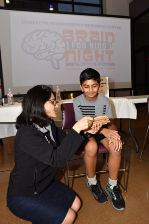 a YOung boy sitting in a char being shown an experiment by a woman in a black dress